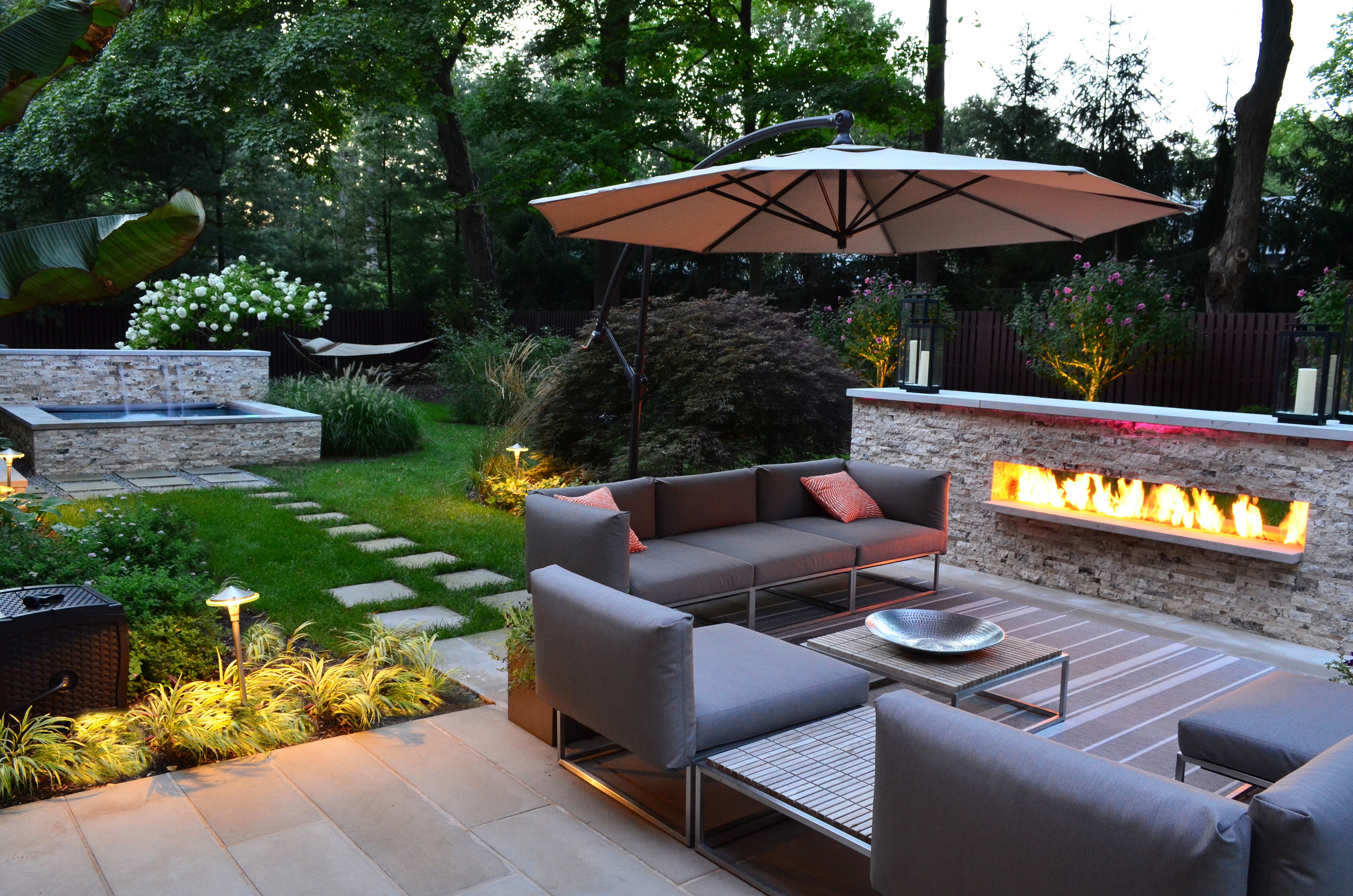 Charming-Modern-Patio-With-Gray-Stone-Outdoor-Fireplace-Also-Cream-Umbrella-As-Well-As-Beautiful-Garden